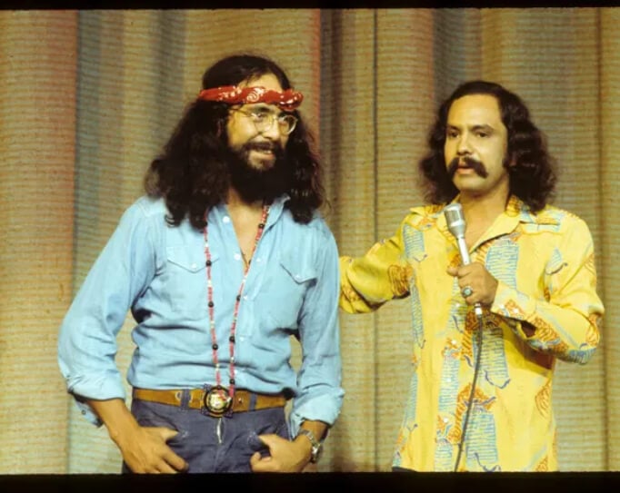 An old picture of Cheech and Chong from the 70s. Tommy in his red bandana, and cheech with his large mustache. Tommy smiles and Cheech holds a microphone.