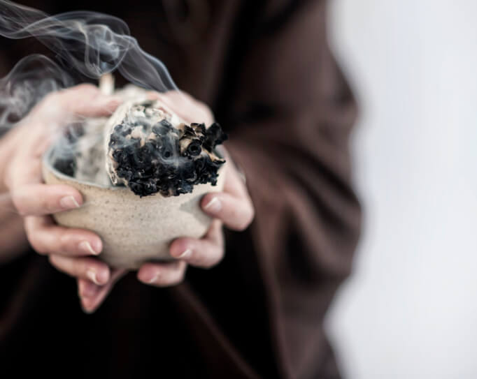 Hands holding a bowl with sage burning inside.