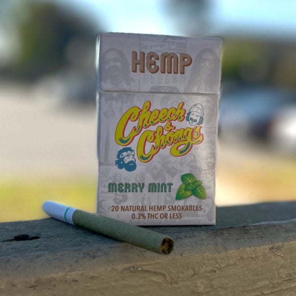 A pack of Granddaddy Grape hemp cigarettes and one cigarette, featuring a grape logo, displayed on a wood surface with soft-focus background.
