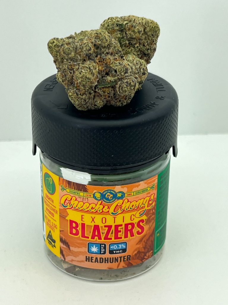 A glass jar labeled "cheech & chong's exotic blazers" containing cannabis with lab results, topped with a rubber lid holding several buds of marijuana. The jar is on a white background.